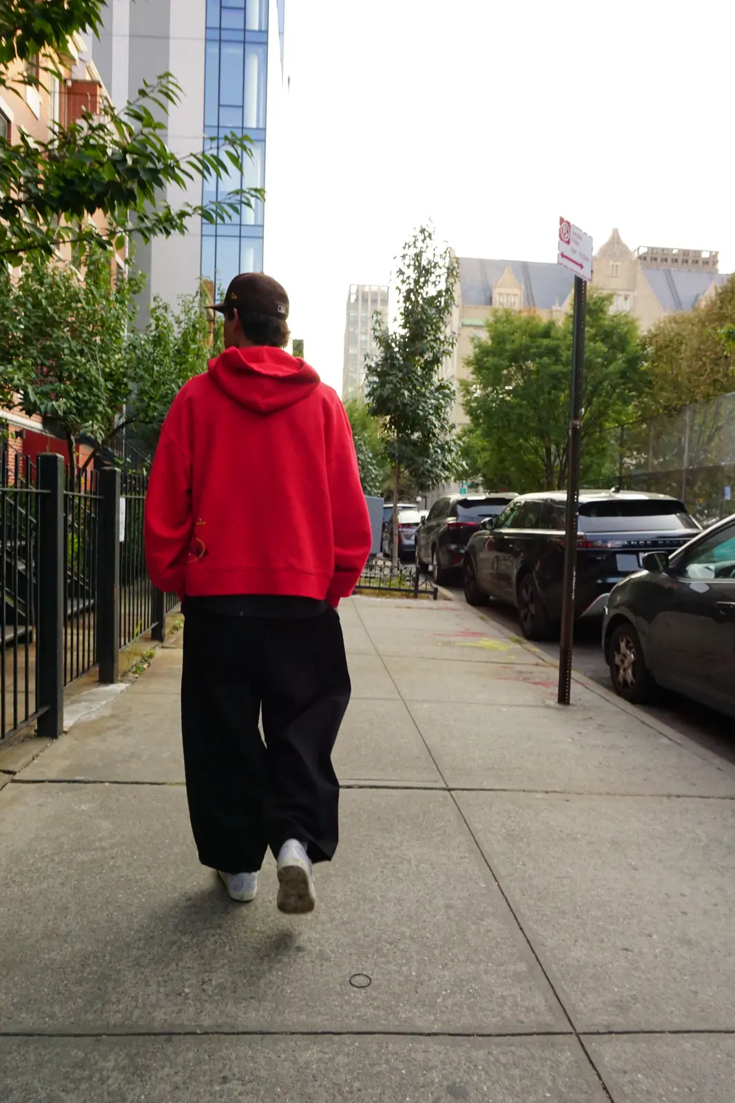 Person in a red hoodie walking along a sidewalk